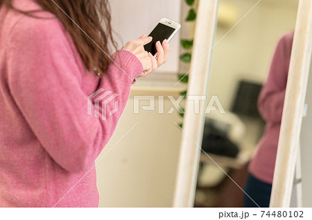 鏡の前でスマホを使うミドル女性の写真素材
