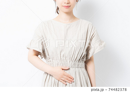 白背景の前に立って、お腹に手を当てる若い女性 白背景の前に立って、お腹に手を当てる若い女性 74482378