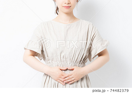 白背景の前に立って、お腹に手を当てる若い女性 74482379