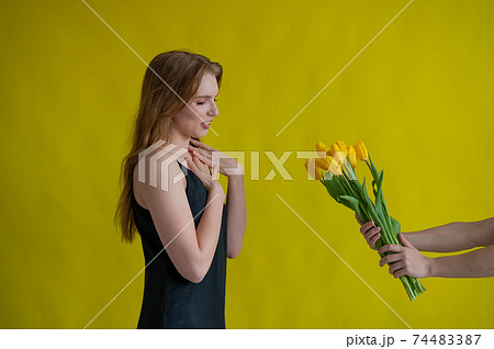 Caucasian woman accepts tulips as a gift on yellow background. 74483387