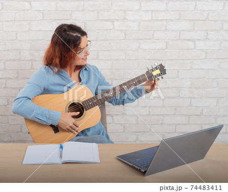 A woman is learning to play the guitar online. Remote music lesson A woman is learning to play the guitar online. Remote music lesson 74483411