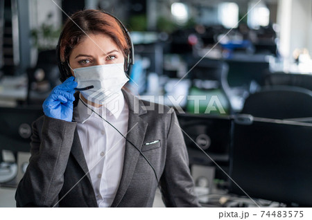 Female call center operator talking to a customer. Woman in mask and gloves at the workplace in the office. Social distance and safety measures to prevent infection. Female call center operator talking to a customer. Woman in mask and gloves at the workplace in the office. Social distance and safety measures to prevent infection. 74483575
