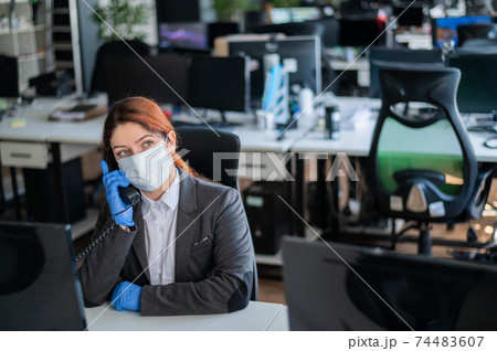A female support operator speaks with a customer on a landline. Woman in mask and gloves at the office desk. The secretary answers the call. A female support operator speaks with a customer on a landline. Woman in mask and gloves at the office desk. The secretary answers the call. 74483607