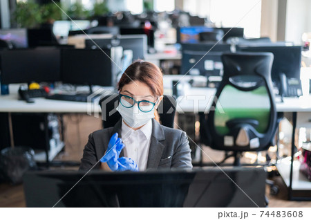 Female office manager in a medical mask puts on gloves at the workplace. A woman in a suit uses personal care products to prevent the spread of the virus. The concept of work during quarantine. Female office manager in a medical mask puts on gloves at the workplace. A woman in a suit uses personal care products to prevent the spread of the virus. The concept of work during quarantine. 74483608