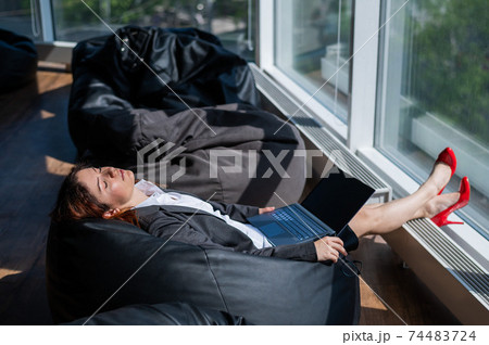 Business lady sleeps sitting in a modern office comfortable bob chair bag. A woman in a suit fell asleep at work on a laptop. Caring for the convenience and comfort of employees. 74483724
