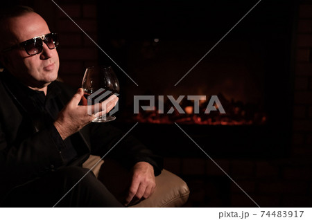 Mature man drinking cognac by the fireplace. 74483917