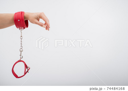 Red leather handcuffs in female hands on a white background. BDSM accessories Red leather handcuffs in female hands on a white background. BDSM accessories 74484168