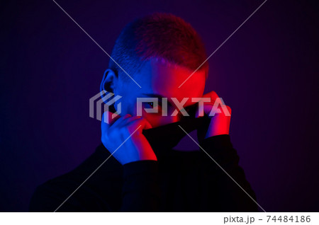 Portrait of a beautiful young woman with short hair in neon light. Girl posing and holding a turtleneck collar 74484186