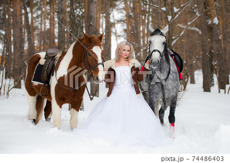 blond woman between horses outdoors in winter nature park. Portrait of a laughing woman with two horses. Friendship and pets concept. blond woman between horses outdoors in winter nature park. Portrait of a laughing woman with two horses. Friendship and pets concept. 74486403