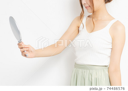 白背景の前で手鏡を見る若い女性 74486576