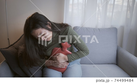 Sick woman with heavy menstrual cramps is applying hot water bag on her stomach 74499484