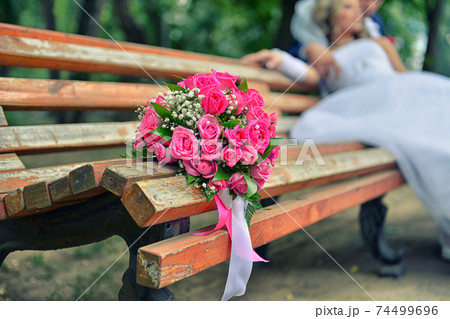bouquet on wooden bench with bride and groom in the background, focus on the flowers bouquet on wooden bench with bride and groom in the background, focus on the flowers 74499696