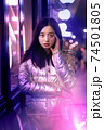 Neon Style. Asian girl in glossy jacket standing on the street in fluorescent violet lights touchign head concerned 74501805