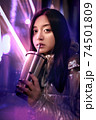 Young adult trendy woman in glowing neon light drinking beverage 74501809