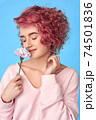 Smiling girl with pink curly hair and nose piercing sniffing carnation flower and enjoying fragrance 74501836