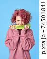 Pretty girl with pink curly hair in pink casual hoodie biting bunch of fresh celery 74501841