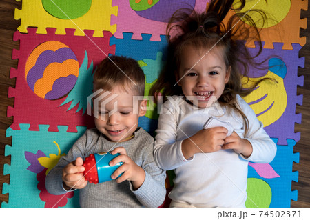 childhood, family friendship, games - close up portrait Two funny joy happy smiling little toddler peschool kids siblings twins brother with sister have fun lie playing on puzzles mat at home indoors 74502371