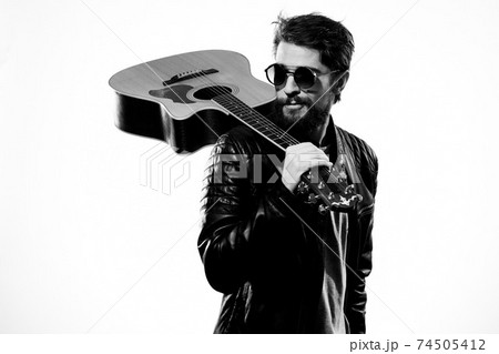 A man holds a guitar in his hands black leather jacket dark glasses music performance light background 74505412