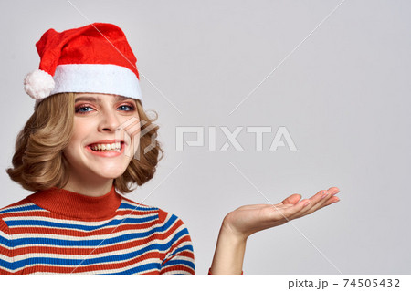 Happy woman in a Christmas cap and a striped sweater gestures with her hands for the New Year holidays Happy woman in a Christmas cap and a striped sweater gestures with her hands for the New Year holidays 74505432