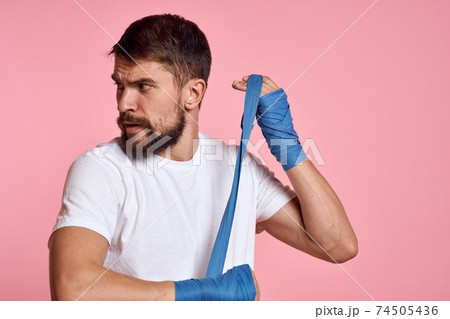 Sporty man in a white T-shirt boxing bandages on the hands of a workout lifestyle pink background Sporty man in a white T-shirt boxing bandages on the hands of a workout lifestyle pink background 74505436