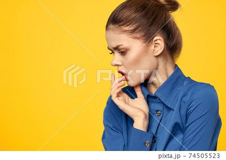 Portrait of a woman in a blue shirt with bright makeup red lips yellow background cropped view 74505523