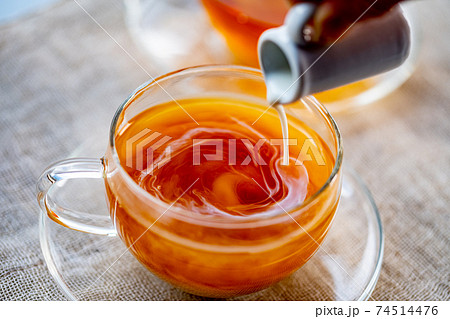 Pouring milk into cup with aromatic tea. Pouring milk into cup with aromatic tea. 74514476
