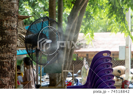 Rotating fan spraying water to the surrounding. Outdoor fan in tropical nature, Thailand. 74518842
