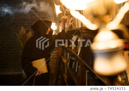 Exorcist in black hood choosing book of spells Exorcist in black hood choosing book of spells 74524151