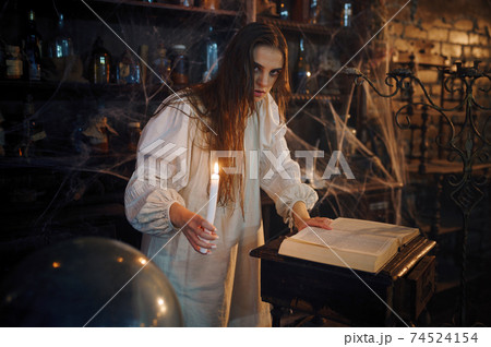 Demonic woman with candle reads book of spells Demonic woman with candle reads book of spells 74524154