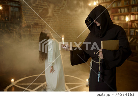 Exorcist in hood casting out demons from a woman Exorcist in hood casting out demons from a woman 74524163