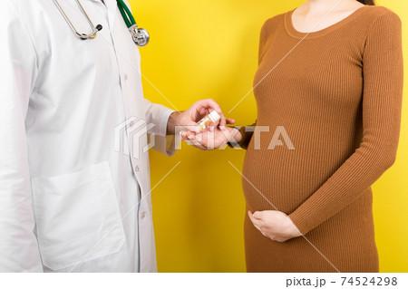 Male gynecologist giving pills to pregnant woman during appointment at colored background. Visit To A Doctor Pregnancy Healthcare And People Concept Male gynecologist giving pills to pregnant woman during appointment at colored background. Visit To A Doctor Pregnancy Healthcare And People Concept 74524298