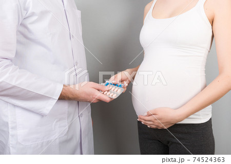 Male gynecologist giving pills to pregnant woman during appointment at colored background. Visit To A Doctor Pregnancy Healthcare And People Concept Male gynecologist giving pills to pregnant woman during appointment at colored background. Visit To A Doctor Pregnancy Healthcare And People Concept 74524363