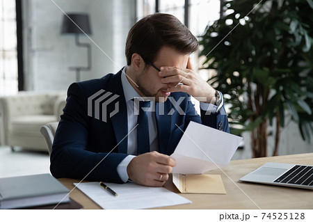 Upset businessman distressed by bad news in letter Upset businessman distressed by bad news in letter 74525128