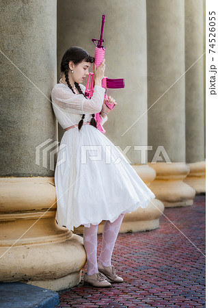 Girl in a white dress with a pink rifle plays airsoft Girl in a white dress with a pink rifle plays airsoft 74526055
