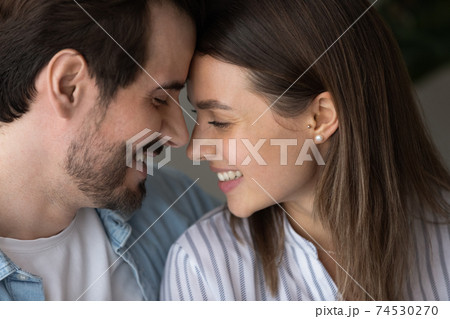 Young couple smiling leaning heads to one another whispering confessions Young couple smiling leaning heads to one another whispering confessions 74530270