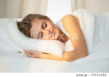 Beautiful young woman sleeping while lying in bed comfortably and blissfully Sunbeam dawn on her face 74531589