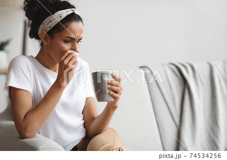 Ill millenial lady holding mug and cleaning nose with napkin Ill millenial lady holding mug and cleaning nose with napkin 74534256
