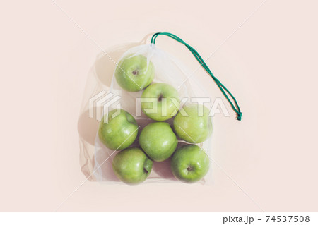 Reusable packaging of products by weight. Apples in a reusable bag close up on a pink background. Reusable packaging of products by weight. Apples in a reusable bag close up on a pink background. 74537508