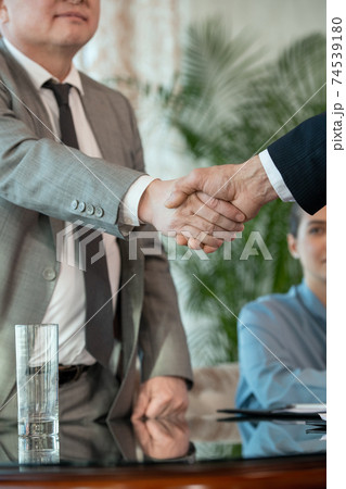 Mature delegate in formalwear greeting his foreign colleague against secretary Mature delegate in formalwear greeting his foreign colleague against secretary 74539180