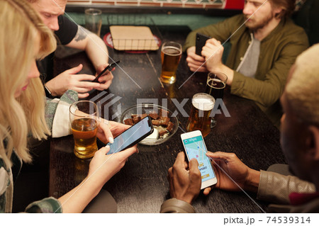 Group of young intercultural friends having beer and scrolling in mobile gadgets 74539314