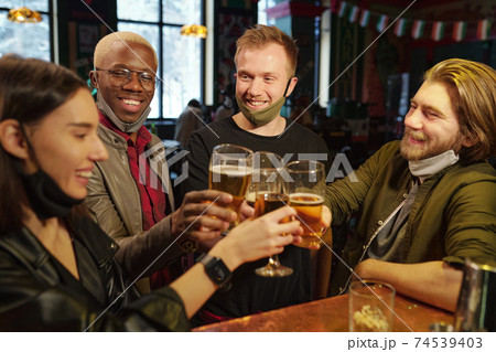 Group of young football fans clinking with glasses of beer over bar counter Group of young football fans clinking with glasses of beer over bar counter 74539403