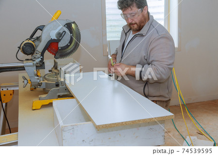 Building contractor worker using measuring and marking a board before cutting wooden shelf 74539595