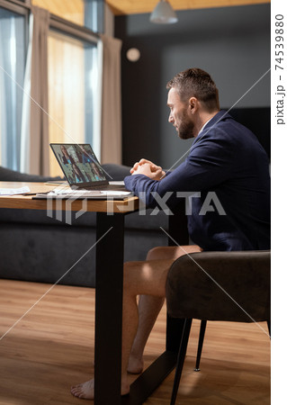 Young businessman in dark blue jacket and underpants sitting in front of laptop Young businessman in dark blue jacket and underpants sitting in front of laptop 74539880