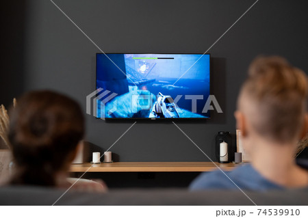 Back view of two kids sitting in front of tv set and playing video game at home Back view of two kids sitting in front of tv set and playing video game at home 74539910