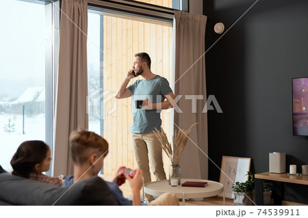 Young relaxed businessman having drink and talking on mobile phone by window Young relaxed businessman having drink and talking on mobile phone by window 74539911