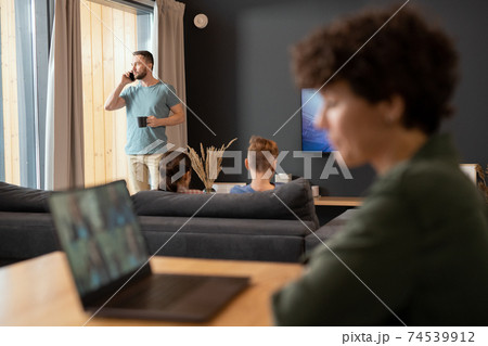 Young businessman standing by window, having drink and talking on mobile phone Young businessman standing by window, having drink and talking on mobile phone 74539912