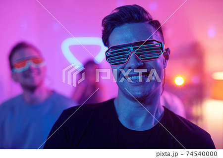 Young smiling man in casualwear and disco eyeglasses looking at you at party Young smiling man in casualwear and disco eyeglasses looking at you at party 74540000