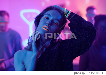 Young woman with glamorous neon makeup standing against her friends at party Young woman with glamorous neon makeup standing against her friends at party 74540001