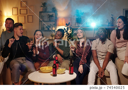 Group of young intercultural friends singing karaoke while sitting on couch Group of young intercultural friends singing karaoke while sitting on couch 74540025