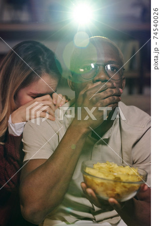 Shocked guy of African ethnicity covering mouth by hand while watching movie Shocked guy of African ethnicity covering mouth by hand while watching movie 74540026